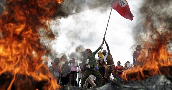 Members of Brazil's Landless Worker Movement or MST hold a flag up by burning tires on a highway in Brasilia.
