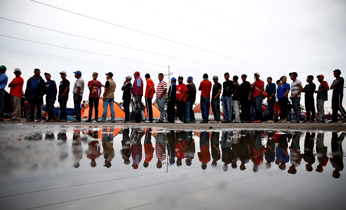 Migrants stand in a line to receive cups of coffee while they wait for buses to take them to Tijuana.