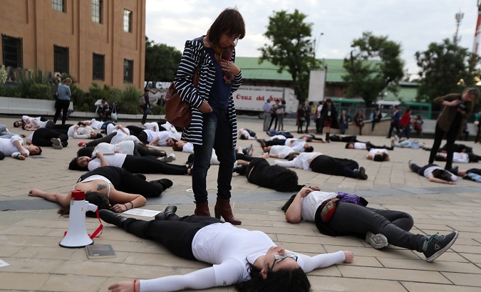 Women lie on the floor pretending to be dead, next to placards with information on murdered women, during a performance against femicide in Santiago, Chile.