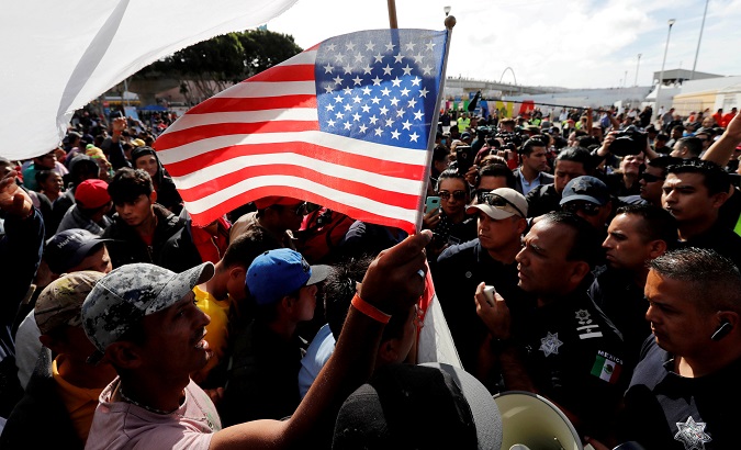 Central American caravan member holds a U.S. flag as the group of asylum seekers negotiate with Mexican police members at the El Chaparral port of entry crossing between Mexico and the United States in Tijuana, Mexico November 22, 2018.
