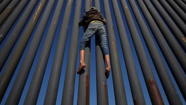 An asylum seekers from Central America Exodus climbs metal border fence between Mexico and the United States, in Tijuana, Mexico, November 18, 2018