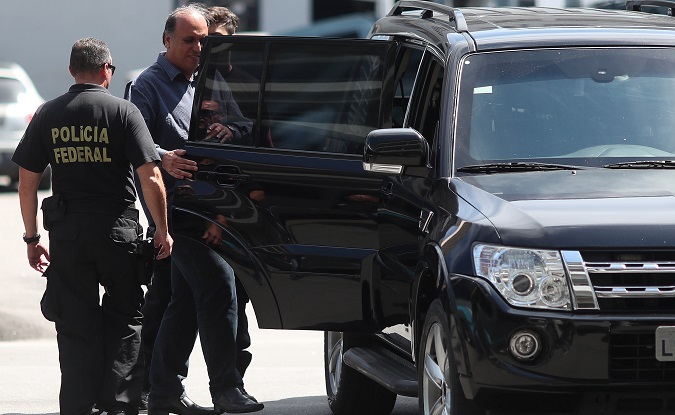 Rio de Janeiro governor Luiz Fernando Pezao is escorted by a policeman at the Federal Police headquarters in Rio de Janeiro, Brazil November 29, 2018.