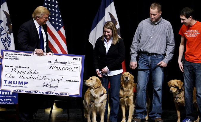 U.S. Republican presidential candidate Donald Trump presents a mock check representing $100,000 to members of the Puppy Jake Foundation in Davenport.