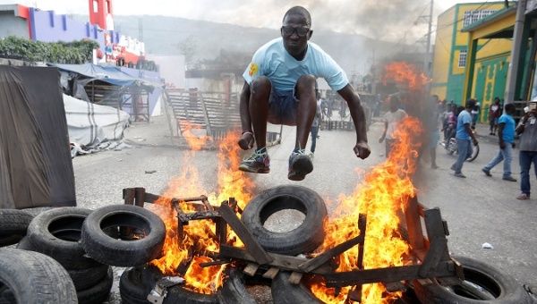 A protester jumps over a burning barricade during a protest against the government in the streets of Port-au-Prince, Haiti, Feb. 10, 2019.