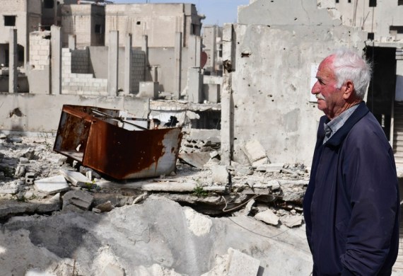 80-year-old Naim Louis stands on the porch of his shattered house in Homs city in central Syria, March 11, 2021.