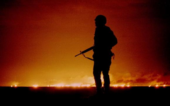 A U.S. soldier stands night guard as oil wells burn in the distance in Kuwait, just south of the Iraqi border Feb. 26, 1991.