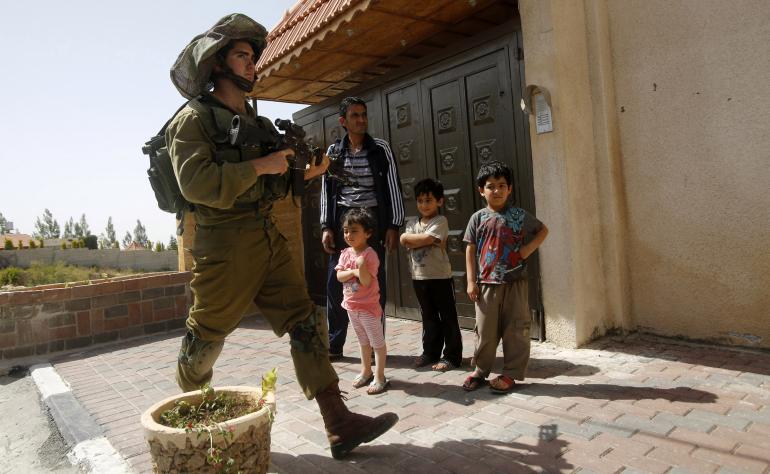 An Israeli soldier patrols as Palestinians stand outside their house in the West Bank City of Hebron June 20, 2014.