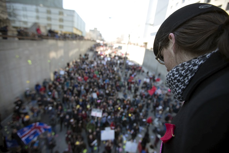 A student wearing the red square watches as thousands march during a student-led protest against the provincial government's austerity measures in Montreal, April 2, 2015.