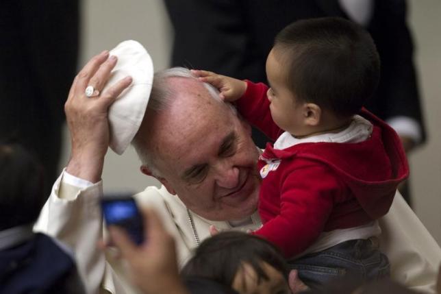 Pope Francis has his skull cap removed by a child during an audience with children assisted