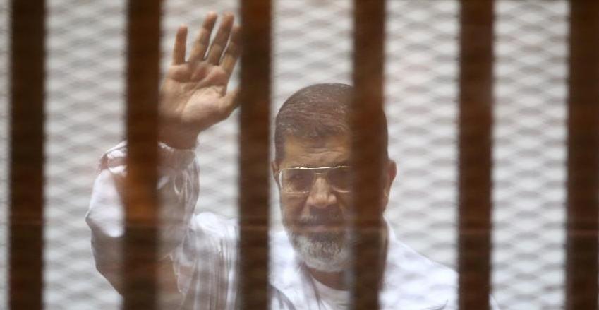 Egypt's deposed president Mohamed Morsi waves inside the defendant’s cage during an earlier court hearing at the police academy in Cairo, on December 7, 2014.