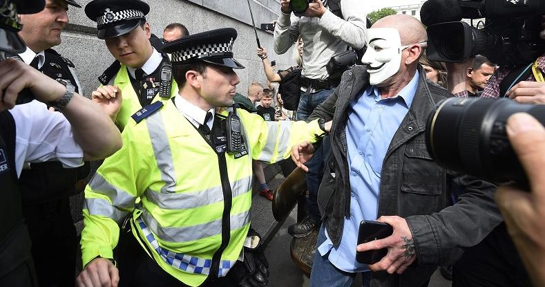 Police confront a demonstrator in a mask during protests in London after the Queen officially opened parliament, May 27, 2015.