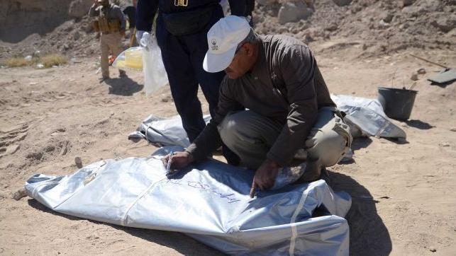 A member from the Iraqi forensic team writes on the body bag of remains exhumed from a mass grave.