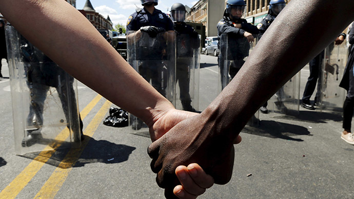 Members of the community hold hands in front of police officers in riot gear in Baltimore.