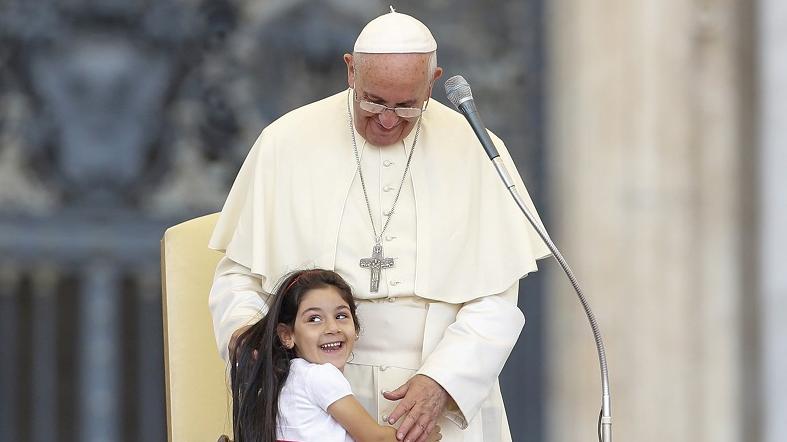 A child smiles as she embraces Pope Francis in St. Peter's square at the Vatican City, June 14, 2015.