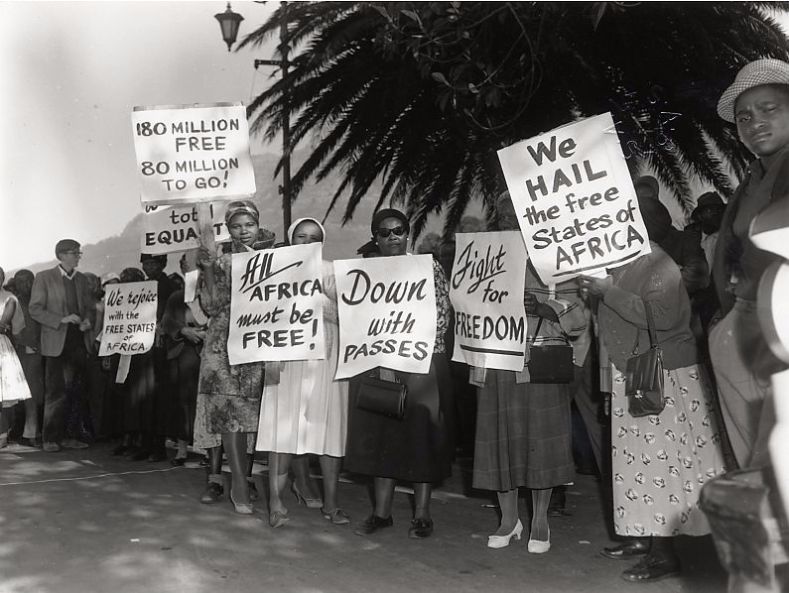 On Africa Day, 1962, a group of women hold signs in protest of oppression in South Africa while other African countries gain their independence. One sign reads: 