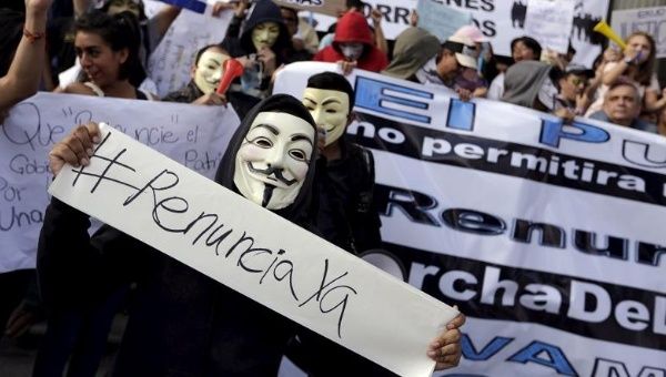 Masked Guatemalan protesters demonstrating against government corruption carry a sign saying 