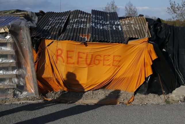 Shadows from migrants are cast on a makeshift shelter with the written word ''Refugee'' in Calais, France, April 30, 2015.