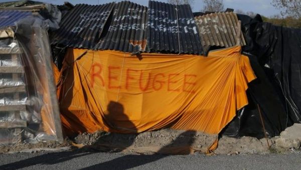 Shadows from migrants are cast on a makeshift shelter with the written word ''Refugee'' in Calais, France, April 30, 2015.