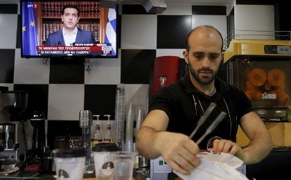 A waiter prepares coffee as the image of Greek Prime Minister Alexis Tsipras is seen on television during a live television address in Athens, Greece, July 1, 2015.