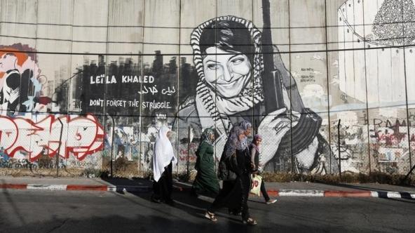 Palestinian women walk past graffiti on Israel’s illegal barrier as they walk towards an Israeli checkpoint in the West Bank town of Bethlehem, during the holy month of Ramadan July 26, 2013.