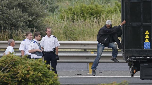 French policemen ask a migrant to get out of the trailer of a truck he climbed in, during an attempt to make a clandestine crossing to England through the Channel tunnel.