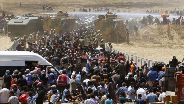 Turkish military use a water cannon to stop Syrian refugees as they wait behind the border fences to cross into Turkey.