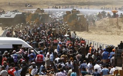Turkish military use a water cannon to stop Syrian refugees as they wait behind the border fences to cross into Turkey.