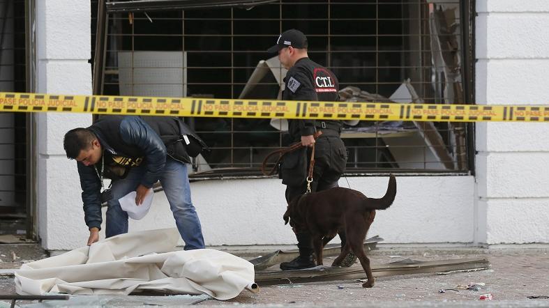 Policemen inspect the site of an explosion with a bomb sniffing dog, in front of the office of the Porvenir pension fund in downtown Bogota July 2, 2015.