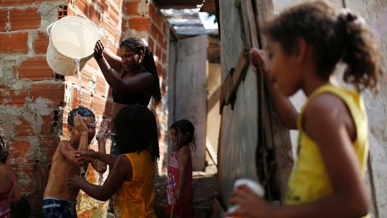 A woman pours water on children to refresh them in the Nova Tuffy slum.