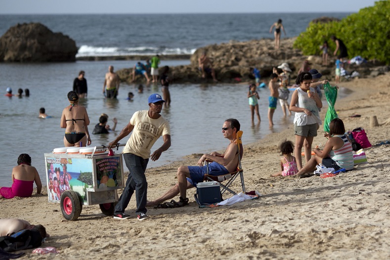 A vendor pulls his ice cream cart past beachgoers on La Peña del Perro beach in San Juan, Puerto Rico, July 18, 2015. While other Caribbean islands have witnessed a steady growth of tourism, the debt crisis in Puerto Rico has contributed to the stagnated tourism industry.