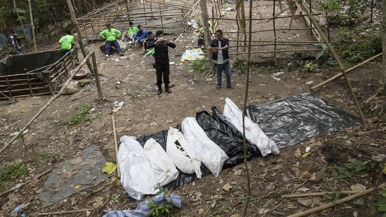 Policemen monitor as forensic experts dig out human remains near an abandoned human trafficking camp in the jungle at Bukit Wang Burma in Malaysia on May 26, 2015.
