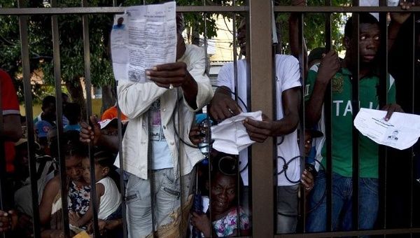 Haitians show their papers while clinging to the fence surrounding the Ministry of Interior and Police.