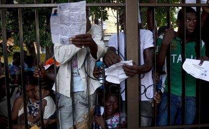 Haitians show their papers while clinging to the fence surrounding the Ministry of Interior and Police.