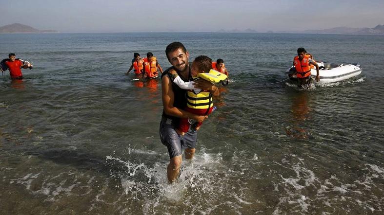 An Iranian migrant cries while carrying his son after a small group of exhausted migrants from Iran arrived by paddling an engineless dinghy from the Turkish coast,  August 15, 2015.