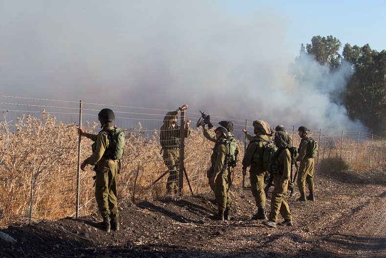 Israeli soldiers stand next to smoke from a fire caused by a rocket attack that they assure was launched from Syria's Golan Heights.
