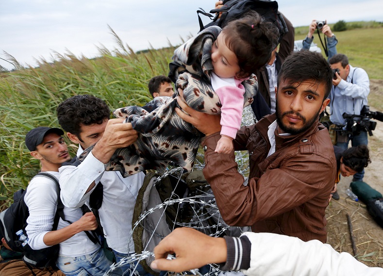 A Syrian migrant hands a girl to another migrant over the Hungarian-Serbian border fence, as they cross into Hungary near Roszke, August 26, 2015.