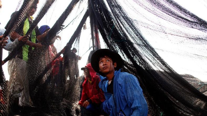 Workers from Myanmar clean a fishing net as they sail out of port of Mahachai.