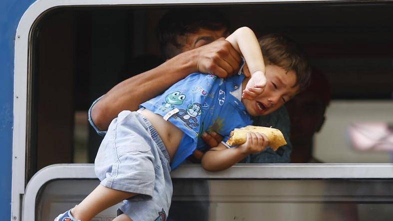 A Refugee pulls a boy inside a train through a window at the Keleti train station in Budapest, Hungary, September 3, 2015.