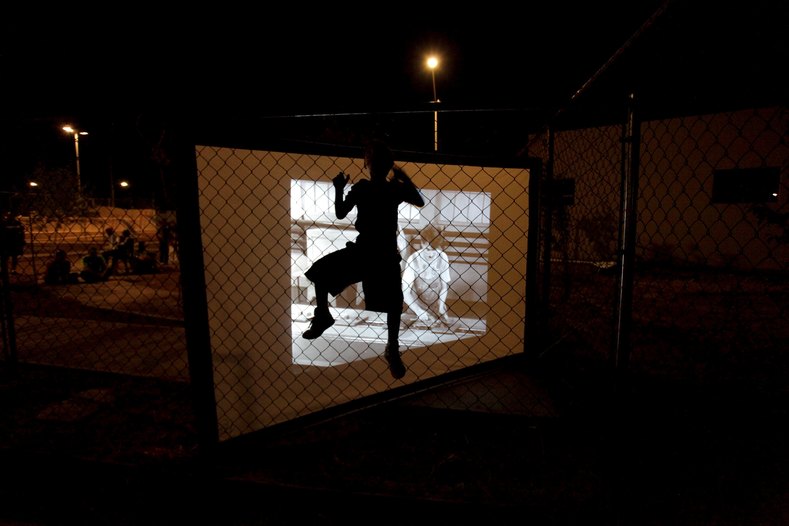 A child climbing a fence is silhouetted by a screen showing a film projected by the Cinecleta, Moviebike, at a park in Saltillo, Mexico, Sept. 6, 2015.