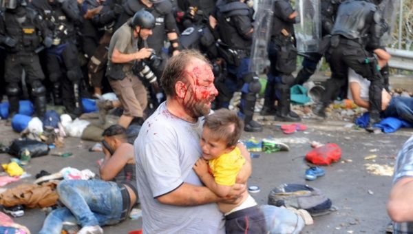 An injured migrant carries a child during clashes with Hungarian riot police at the border crossing with Serbia in Roszke, Hungary. Hungarian riot police used tear gas against crowds of refugees and migrants packed with children and the elderly.