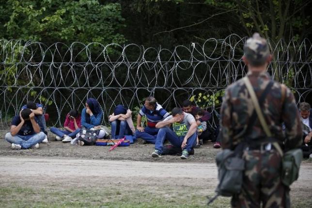 A soldier guards migrants detained after crossing the border from Serbia into Hungary