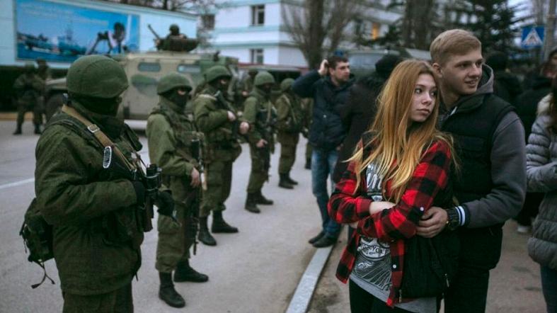 A couple stands next to armed servicemen outside a Ukrainian border guard post in the Crimean town of Balaclava March 1, 2014.