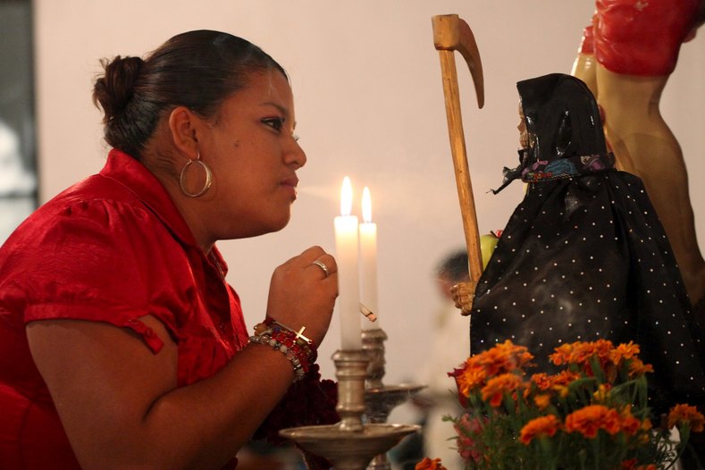 A woman blows smoke from a cigarette towards a figurine of La Santa Muerte (Saint Death) at a shrine during Day of the Dead celebrations also in Ciudad Juarez. 