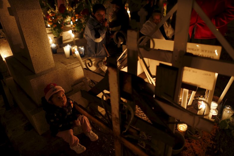 A child sits next to a grave of a relative on the Day of the Dead, at a cemetery of Metepec on the outskirts of Mexico City.