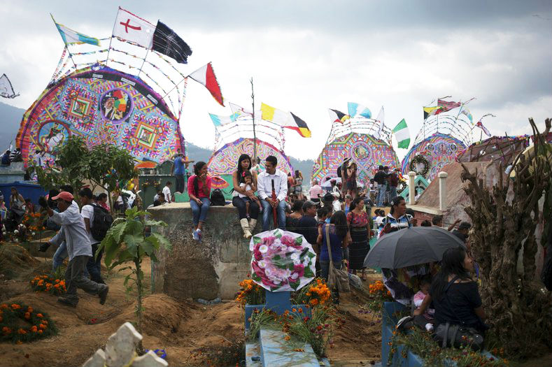 People sit at graveyards in front of giant kites in the cemetery of Santiago Sacatepequez, Guatemala. Dating back 116 years, the tradition of flying kites in the cemetery of of Santiago Sacatepequez, integrates the Catholic feast of All Saints with ancient Mayan practices of honouring the dead. It is believed that the kites connect the living and the dead during the all saints day celebration.