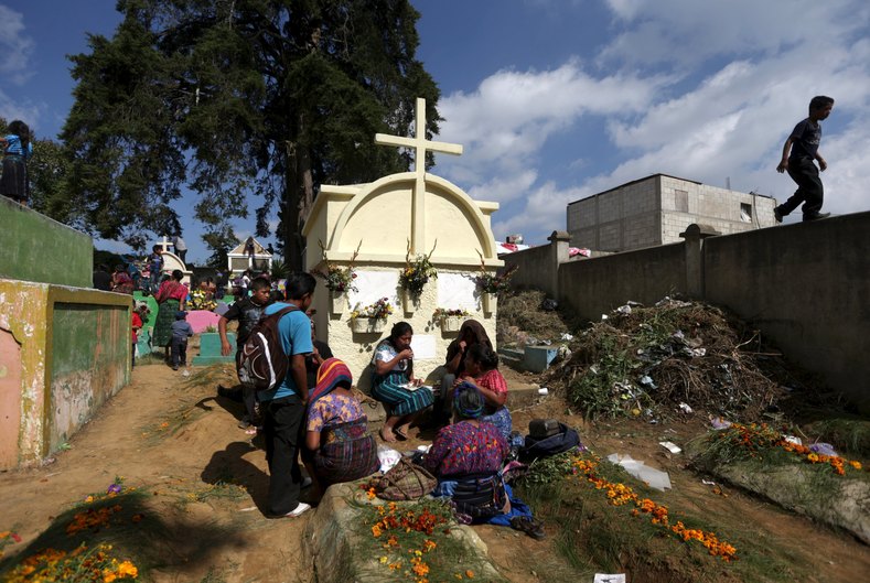 People eat next to a grave during an All Saints celebration with kites in the cemetery of Santiago Sacatepequez, Guatemala, November 1, 2015. Dating back 116 years, the tradition of flying kites in the cemetery of of Santiago Sacatepequez, integrates the Catholic feast of All Saints with ancient Mayan practices of honouring the dead. It is believed that the kites connect the living and the dead during the all saints day celebration.
