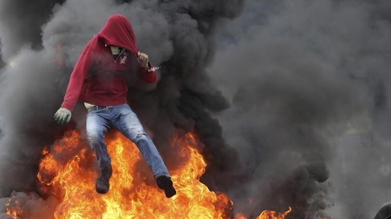 A Palestinian protester jumps over burning tires during clashes with Israeli troops near the Jewish settlement of Bet El, near the West Bank city of Ramallah, Oct. 26, 2015.