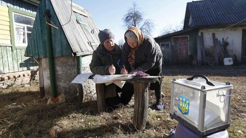 A local resident (R) fills in a ballot brought by an election commission member during a parliamentary election in Horodyshche near Chernihiv, Oct. 26, 2014.