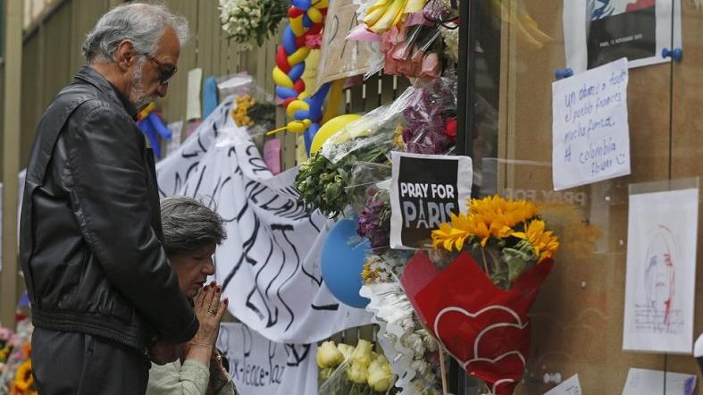 People pray next to tributes offered for victims of the Paris attacks, outside the French embassy in Bogota, Colombia, Nov. 15, 2015.