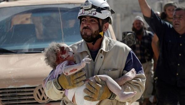 A civil defense member carries an injured baby who was pulled out from under debris in Syria.